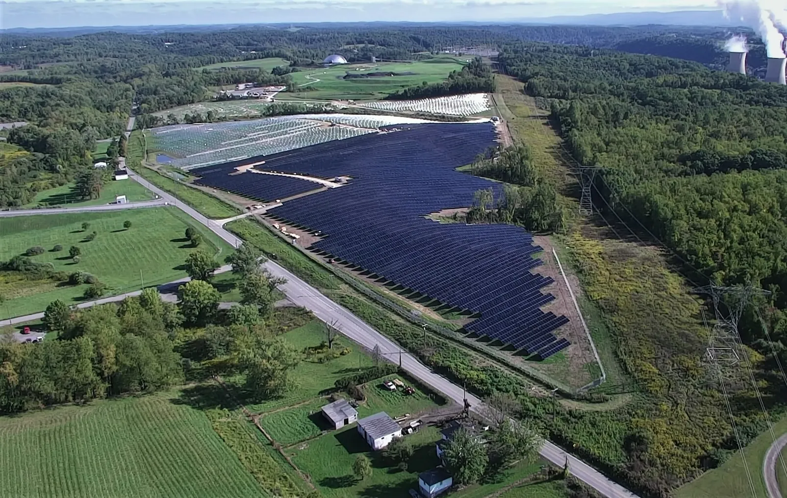 An aerial view of a solar farm next to power lines and trees.