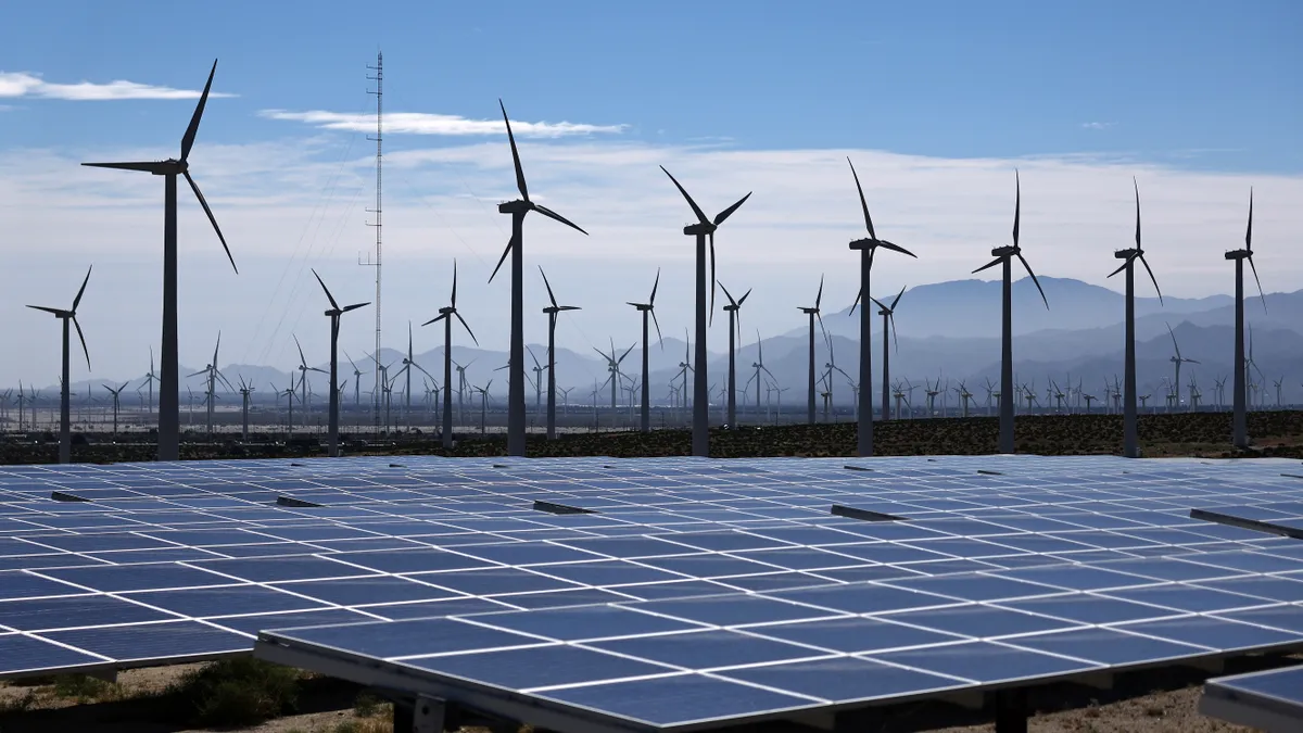 Wind turbines seen behind solar panels at a wind farm.